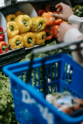 Persona eligiendo pimientos con una cesta de la compra en el supermercado